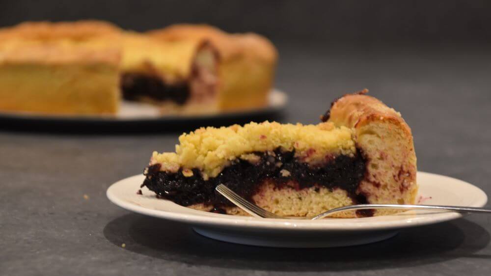 Image of a slice of black currant vlaai, the rest of the vlaai blurred in the background