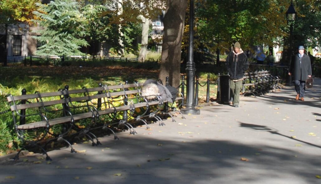 Image of a homeless man sleeping on a bench in a park